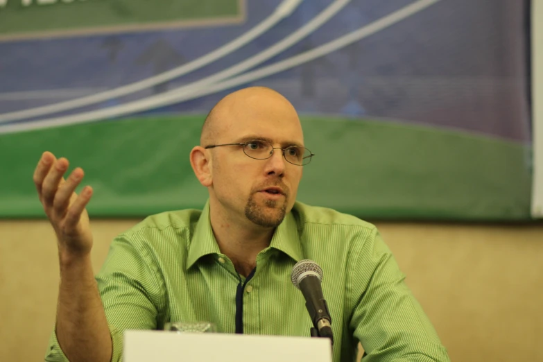 a man in a green shirt and glasses at a microphone