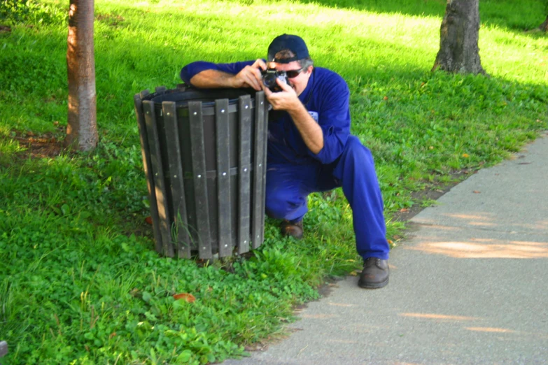 a man crouching down and taking a po of a trash can