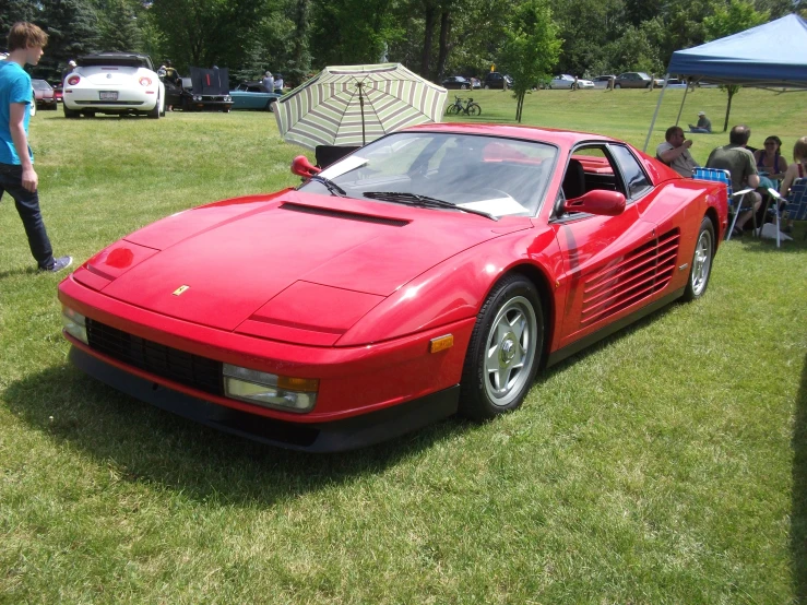 a red ferrari sitting in a field at a car show