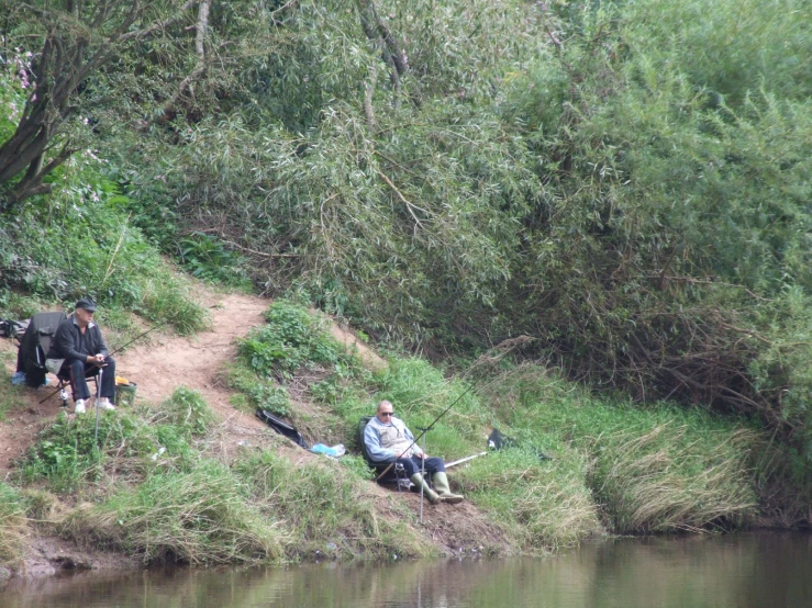 two men are sitting near a river looking at some fish