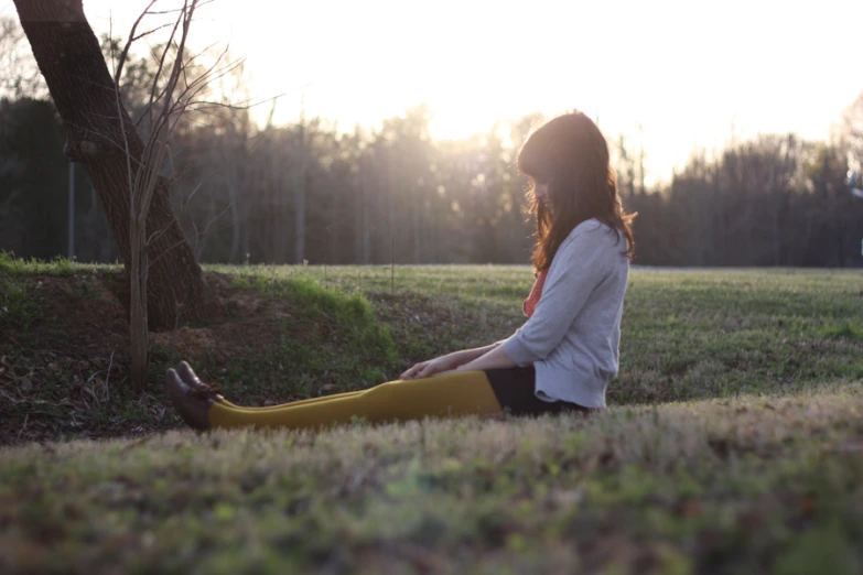 a woman sitting on top of a grass covered field