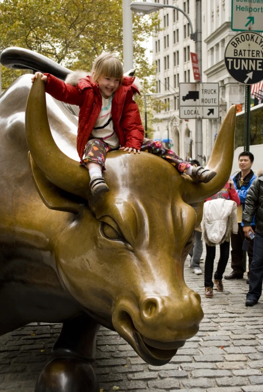 a little girl is sitting on a ss bull statue