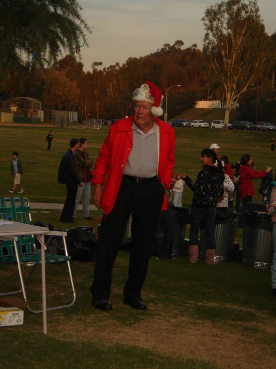 an older man wearing a christmas hat standing near a crowd