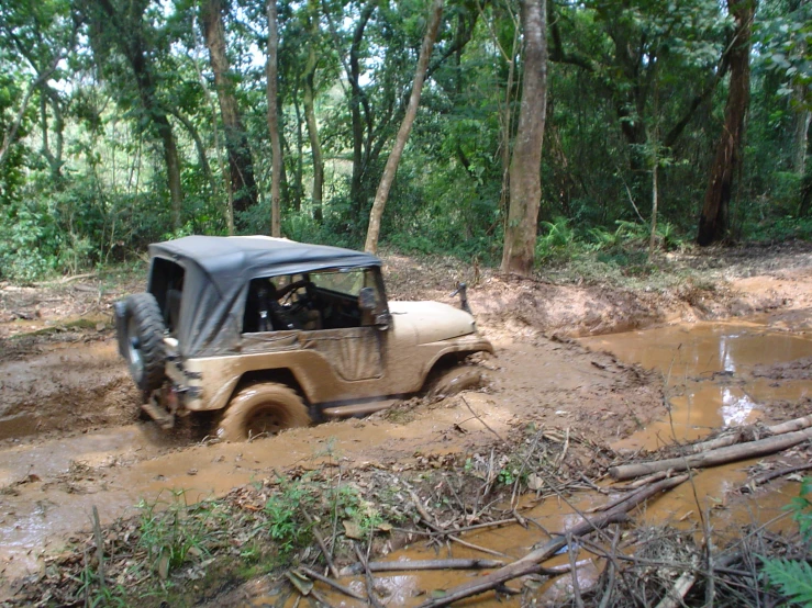 a jeep drives through a muddy dirt trail in the woods