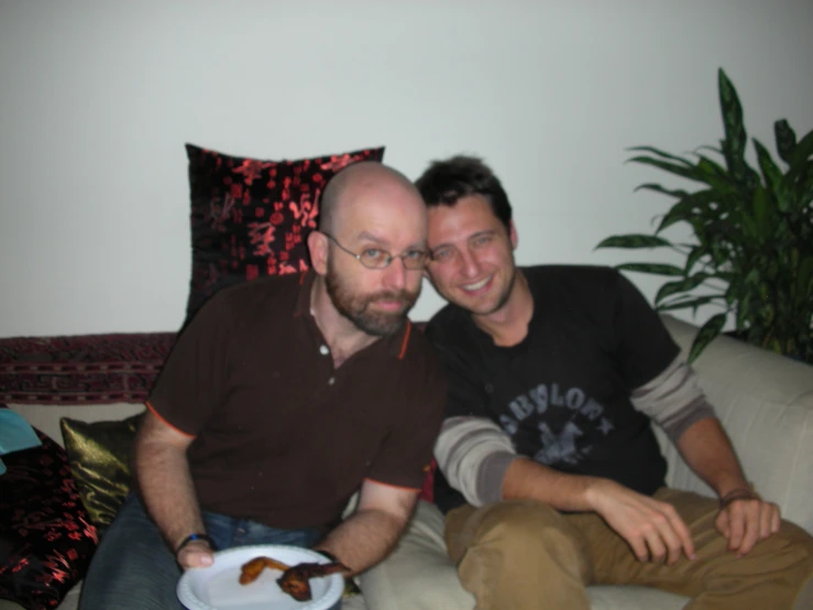 two men sitting on a couch hugging their foreheads