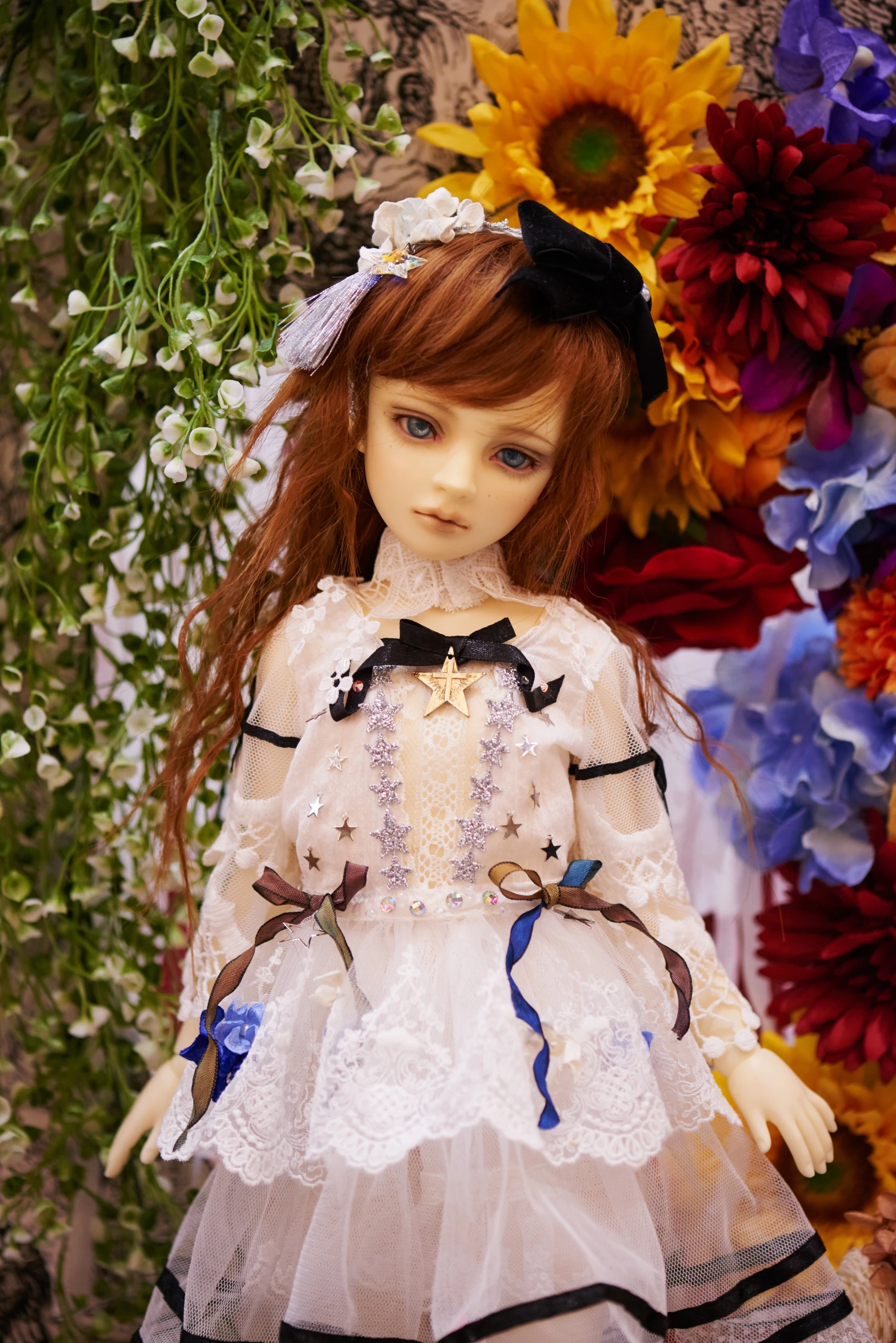 a small doll with long hair wearing a dress in front of flowers