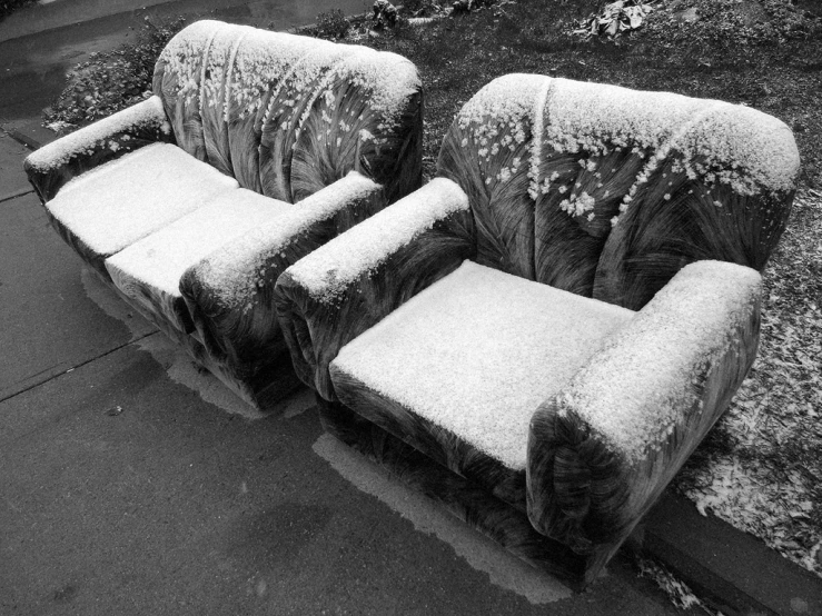 two seats covered in frost sitting in front of a sidewalk