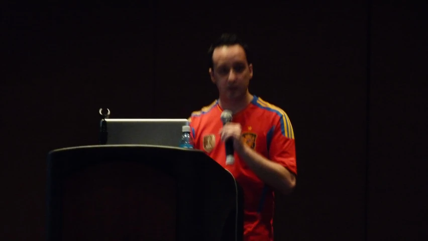 man standing at podium, clapping, in front of screen