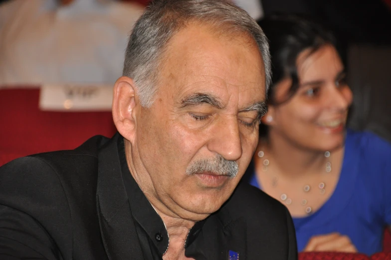 an old man wearing a black suit and red tie