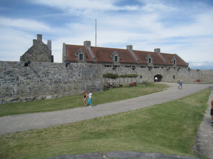 two women are walking down the sidewalk in front of an old stone castle