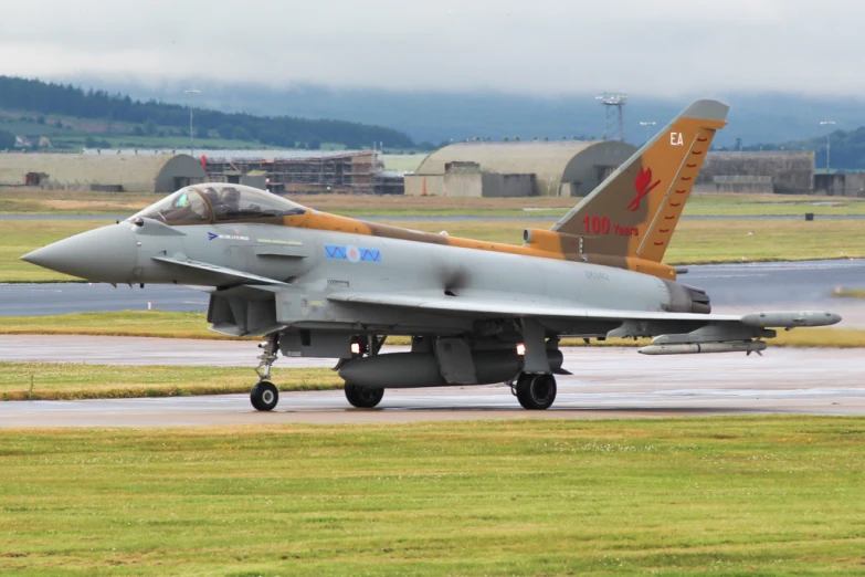 an orange and grey fighter jet sitting on top of an airport runway