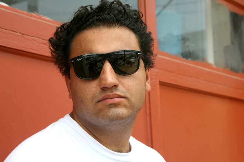 a man with black hair wearing sunglasses in front of a building