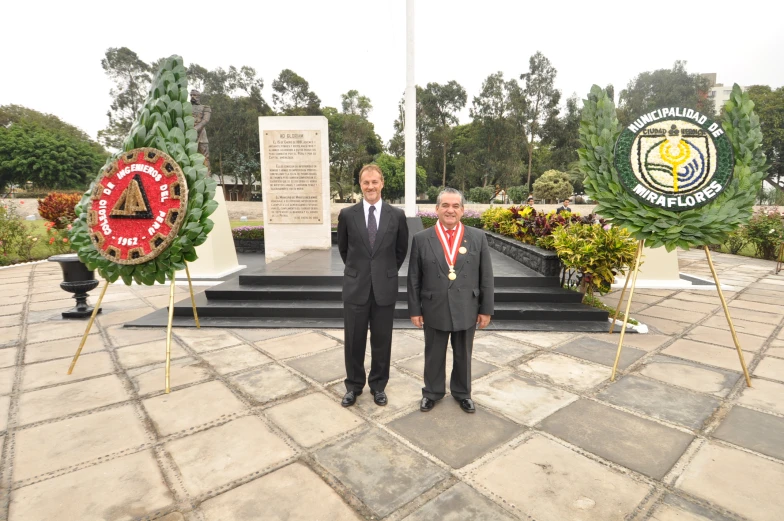 two men in suits are standing at a wreath