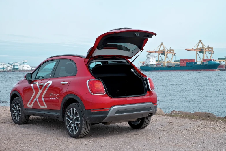 red car with open hood parked next to the ocean