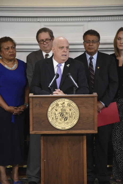 two men and women standing in front of a man speaking on the microphone