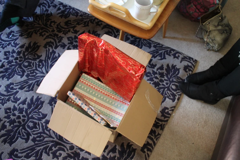 an open cardboard box filled with gift wrap sitting on a rug