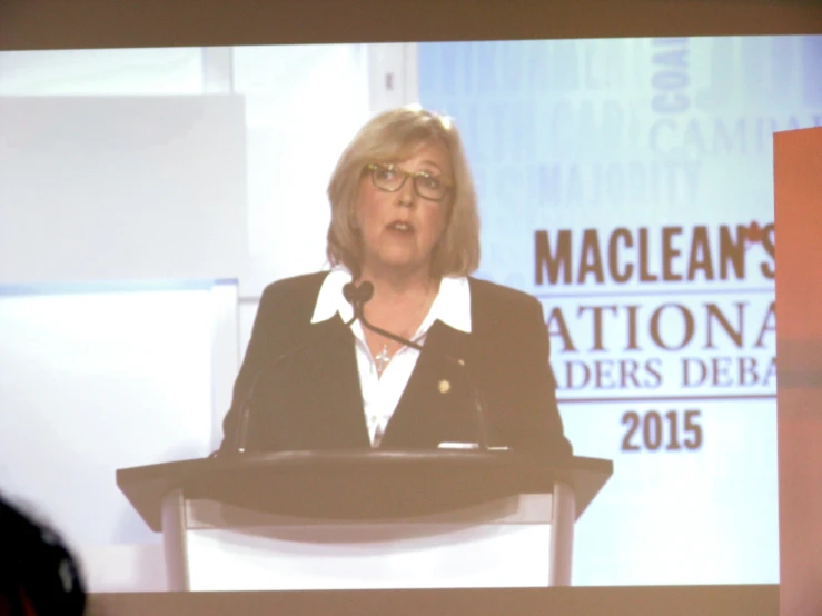 a woman wearing glasses at a podium in front of a screen