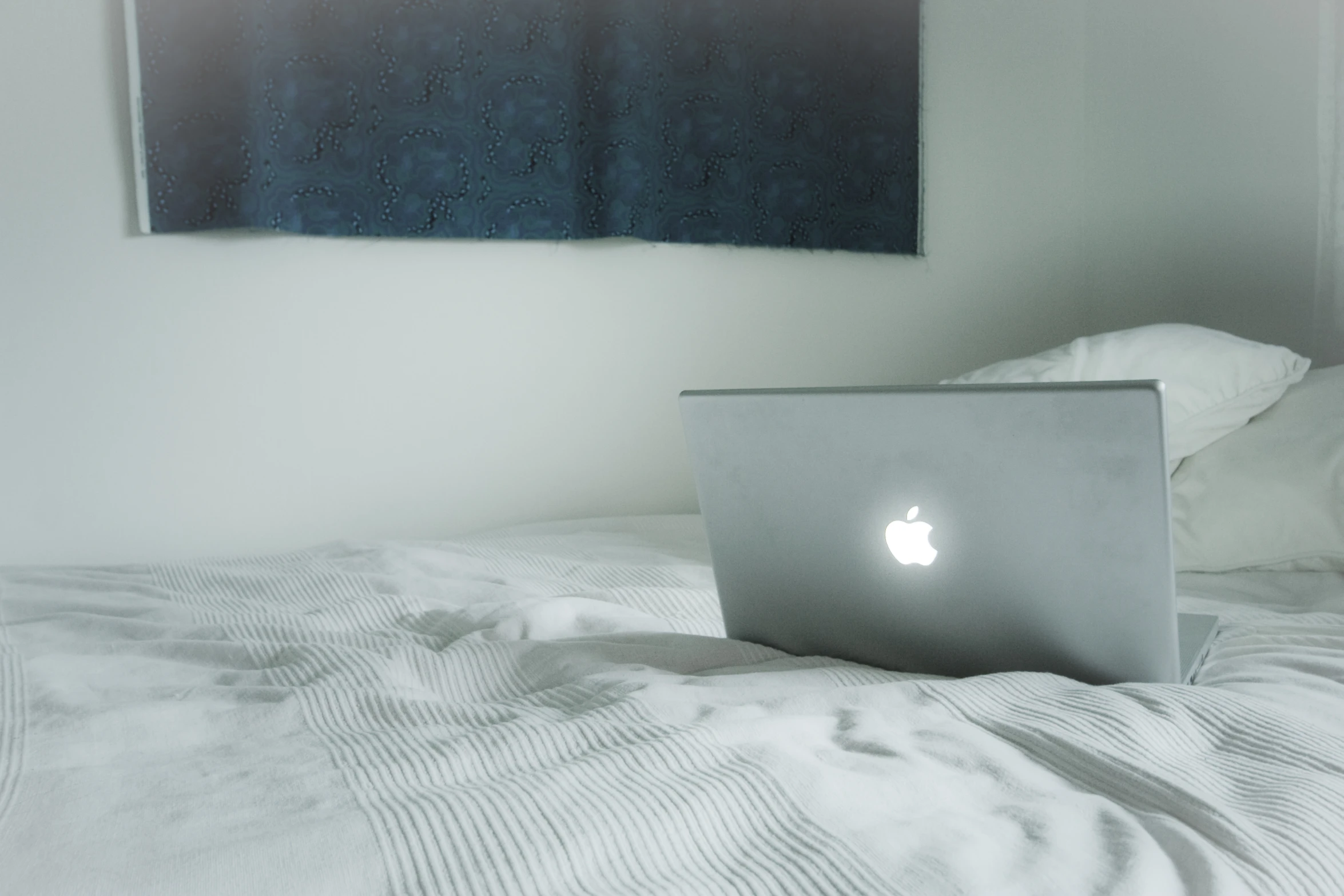 a laptop on a bed near a painting