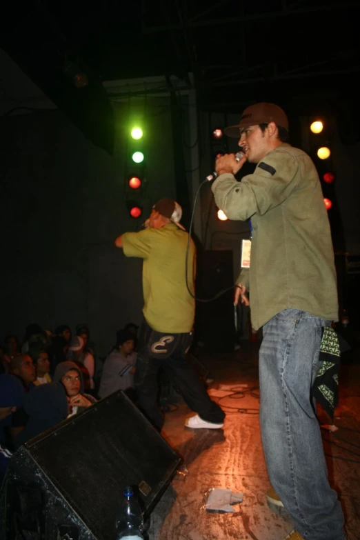 two men on stage singing into microphones with one standing up