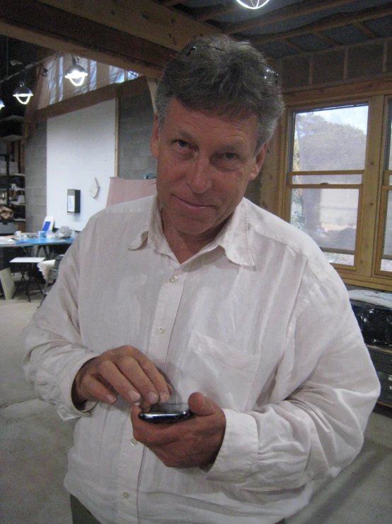 an older man stands in front of the camera, holding his cell phone and looking at it