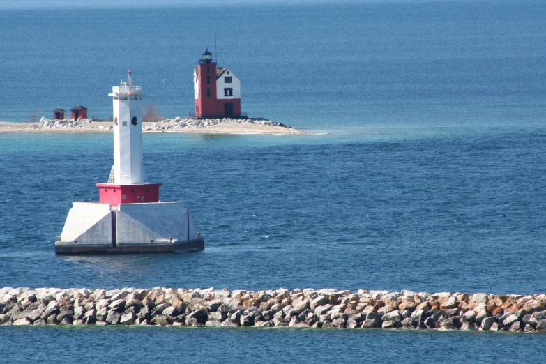 a white and red lighthouse on top of a rocky beach next to water