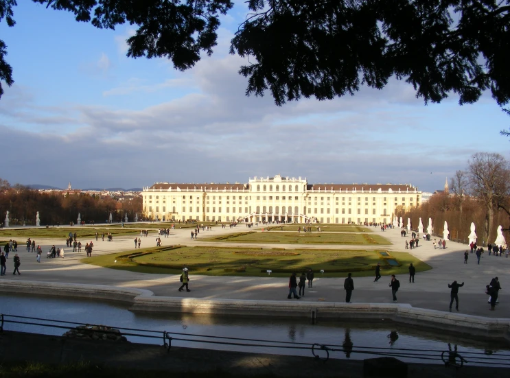 people walk along a water body in front of an old palace