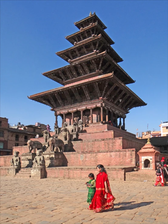 a woman in a red skirt walks next to her child with a pagoda style building behind her