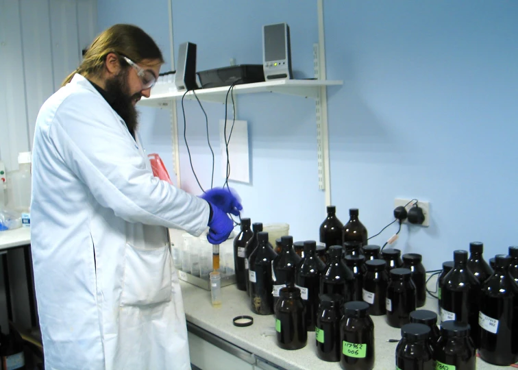 a man in a white lab coat and gloves putting soing into bottles