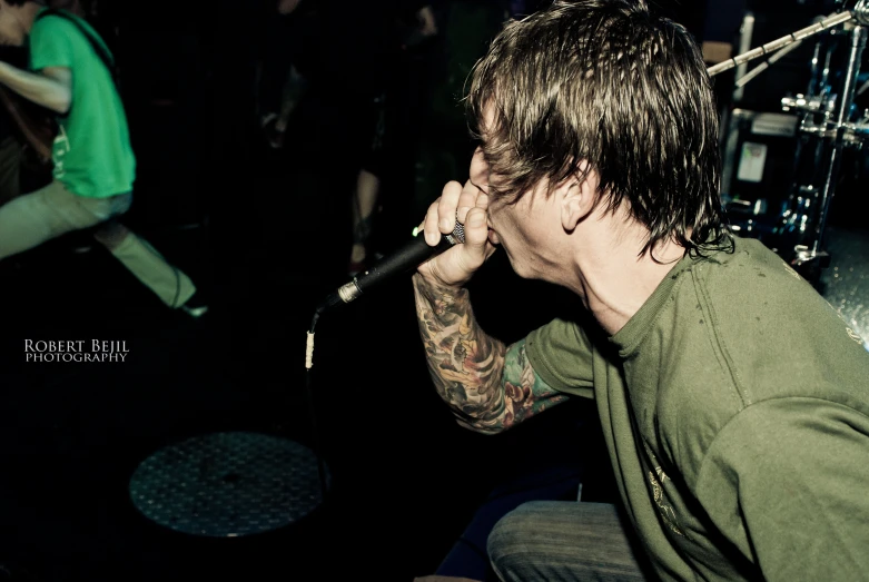 a man sitting and singing on stage with other people