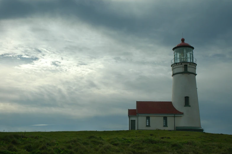 a white light house sitting on top of a grass covered hillside