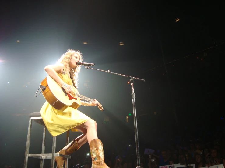 woman with yellow dress and cowboy boots sitting in front of guitar