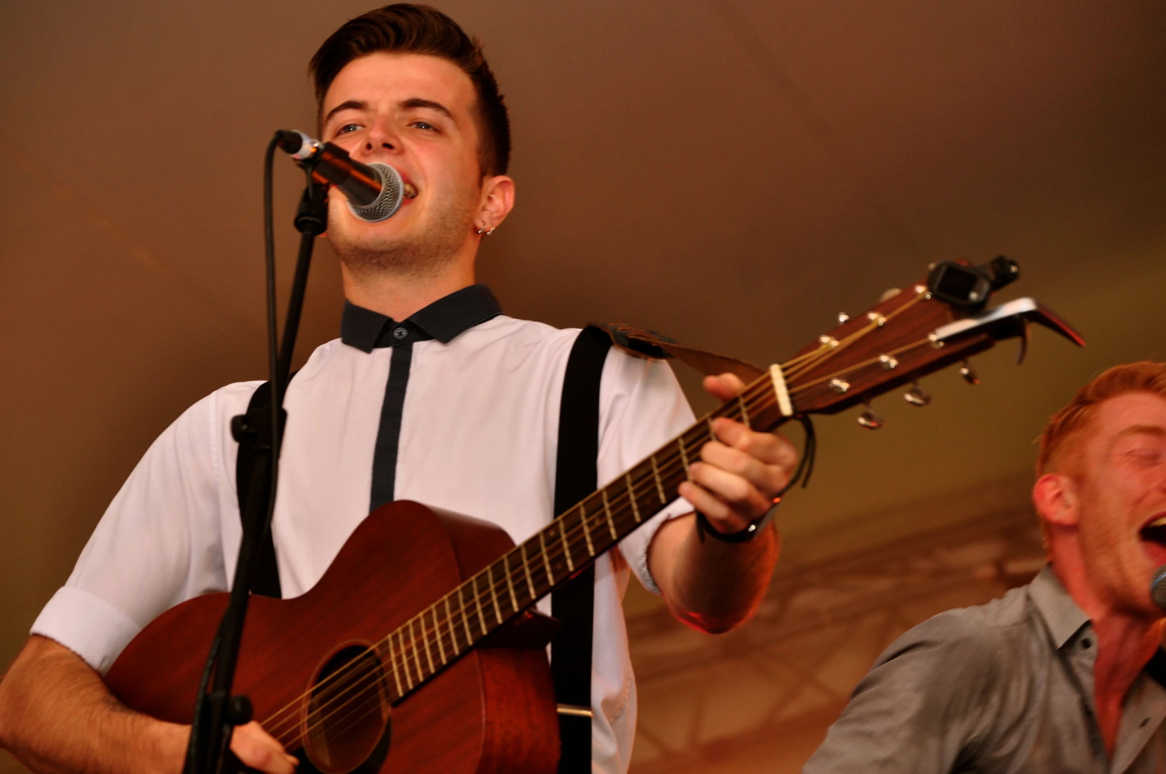 a man holding a guitar sings into a microphone