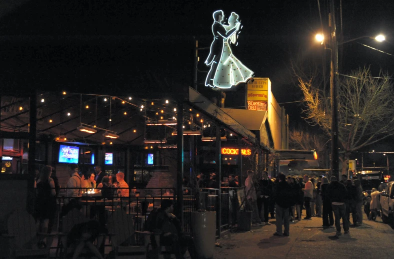 an illuminated sign above a sidewalk covered in people