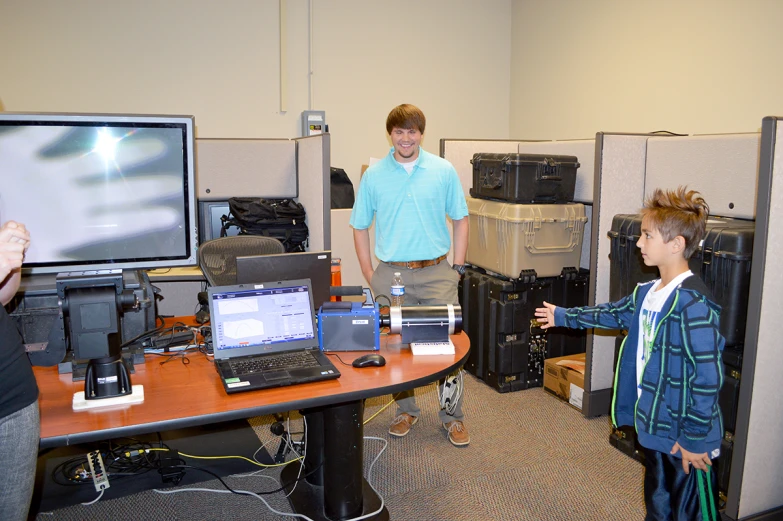 two children standing next to desks with computers on them