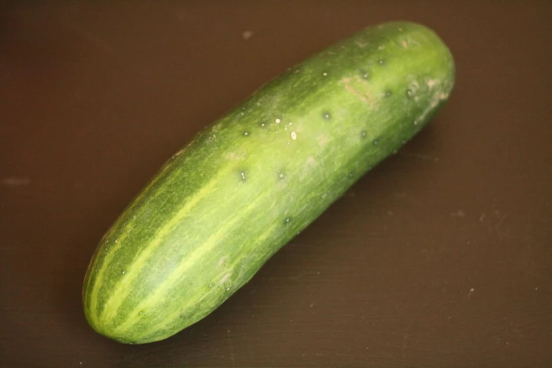 a cucumber laying on a brown table near a knife