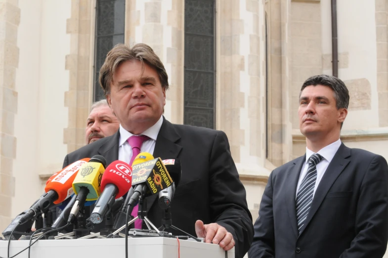 a man in a suit stands next to microphones