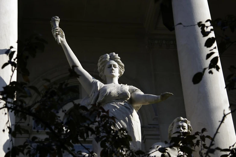 statue of a woman holding up her arms next to three pillars