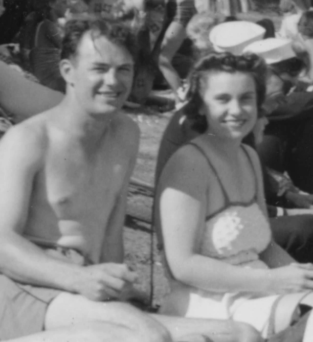 two people sitting on the beach with a crowd behind them