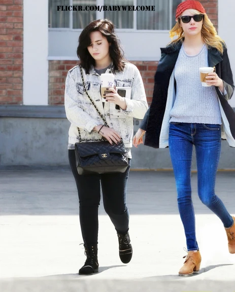 two women walking down a street with a drink and cellphone