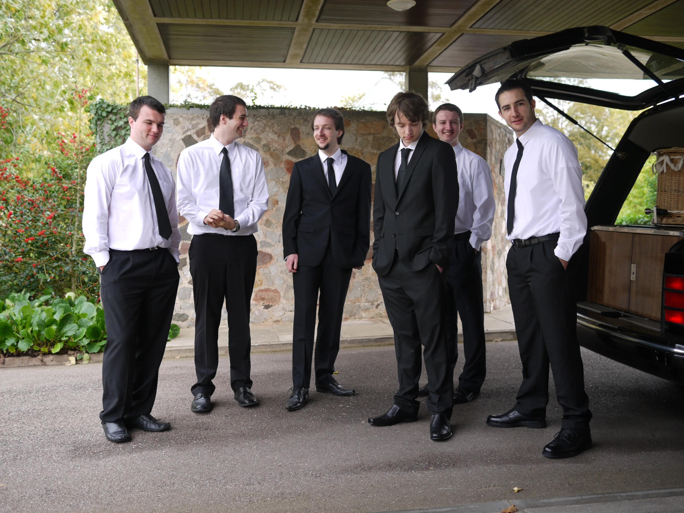 four young men in ties are standing in front of a car