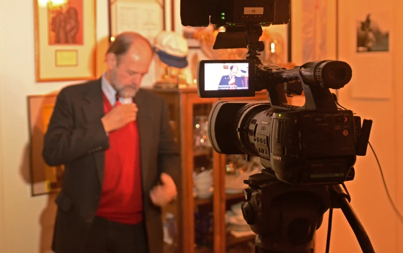 a man in a suit and tie adjusting his tie next to a video camera