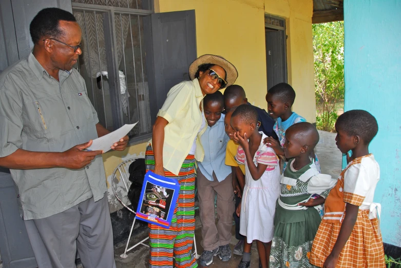 a man stands with a group of children in front of a yellow building