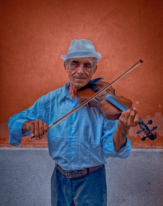 an older man plays the violin against a red wall