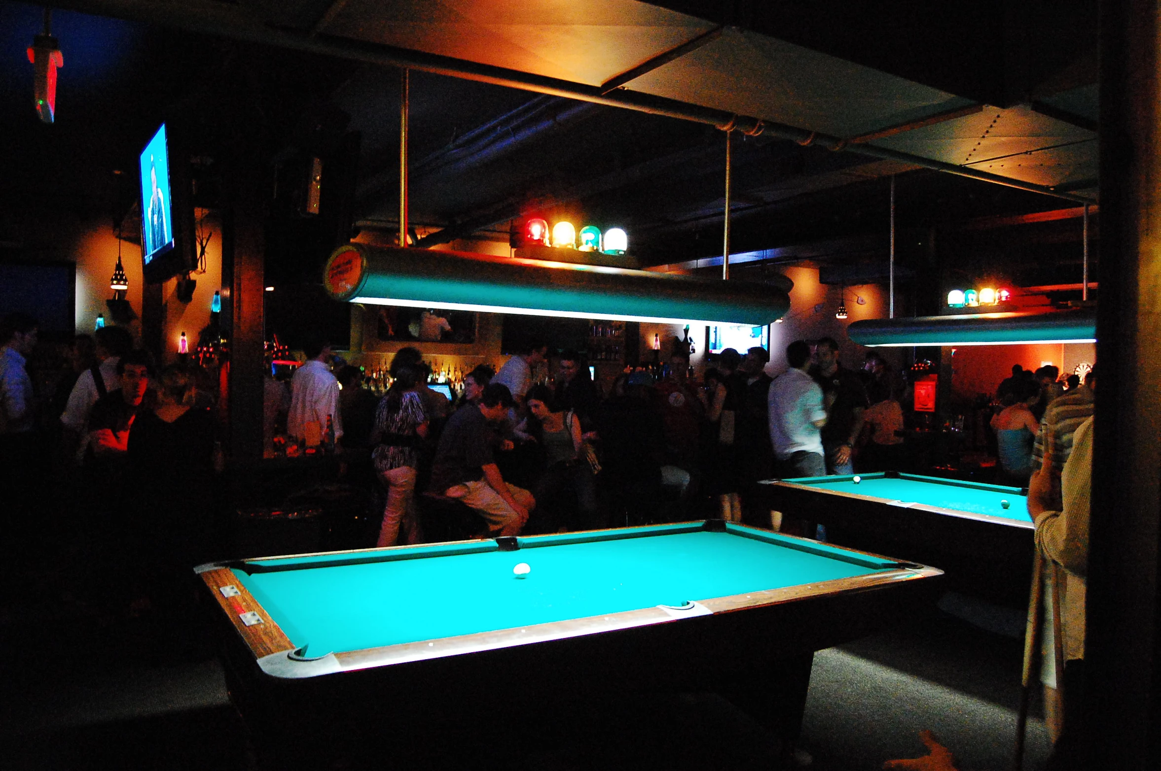 people gathered around billiards tables playing pool in a club