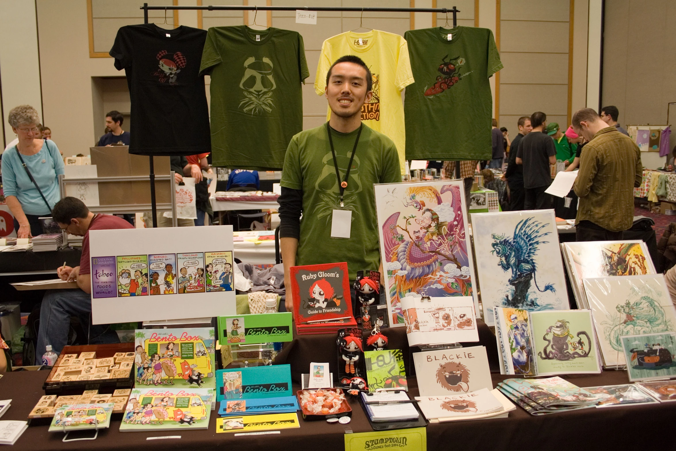 the man is standing by the tables with his assortment of greeting cards