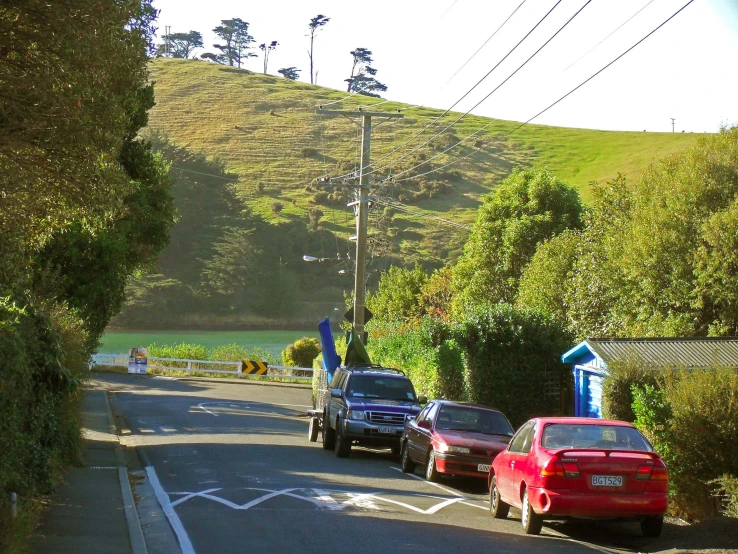three cars are parked along the street, a hill is in the background