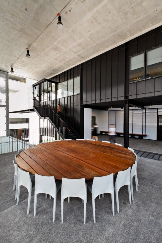 a round wooden table with white chairs under an open spiral staircase