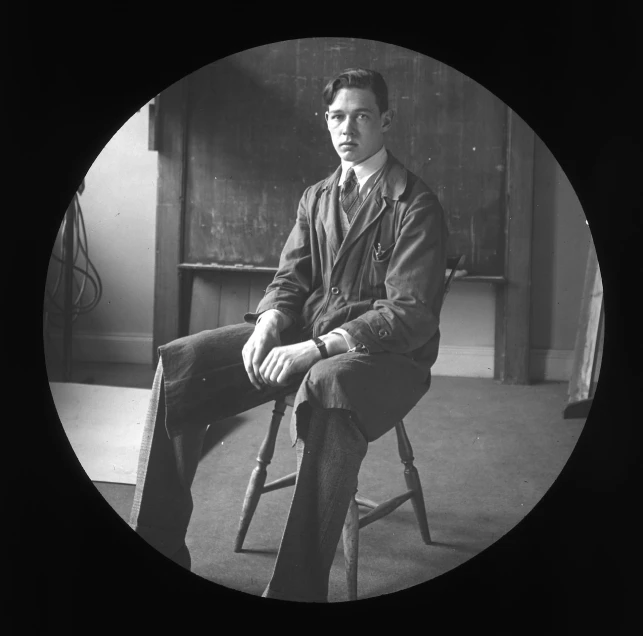 man sitting on chair in large room with chalkboard behind