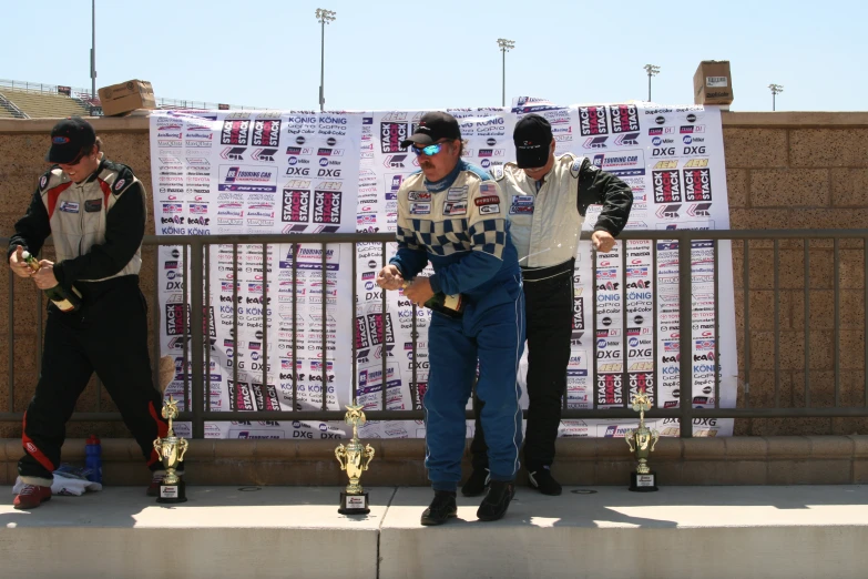 three men in race gear standing on a sidewalk next to trophies