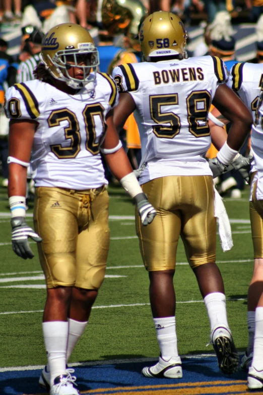 three football players in white and gold uniforms on the field